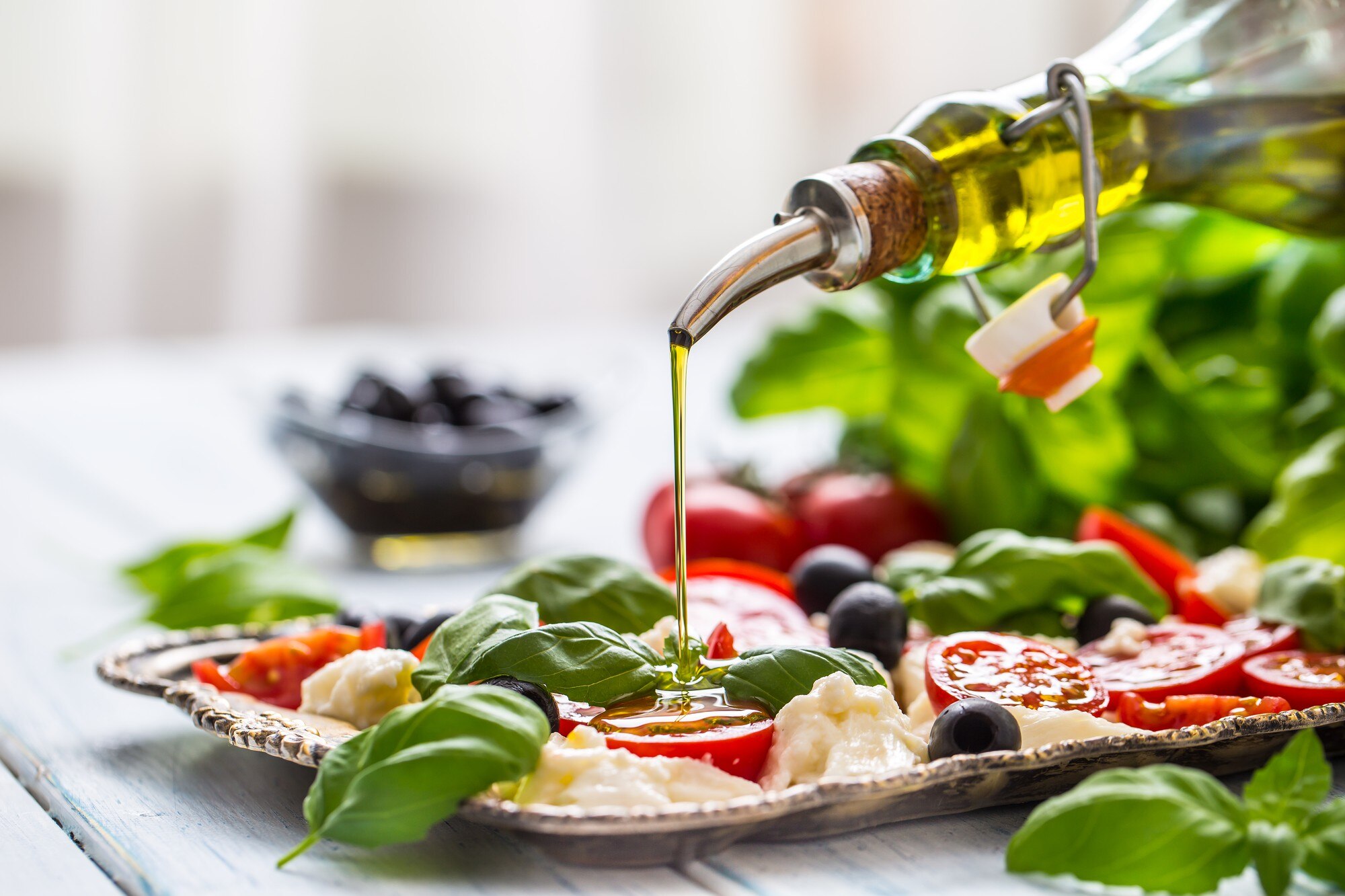 Extra-virgin olive oil being poured over a fresh caprese salad with tomatoes and mozzarella, representing a Mediterranean-style meal