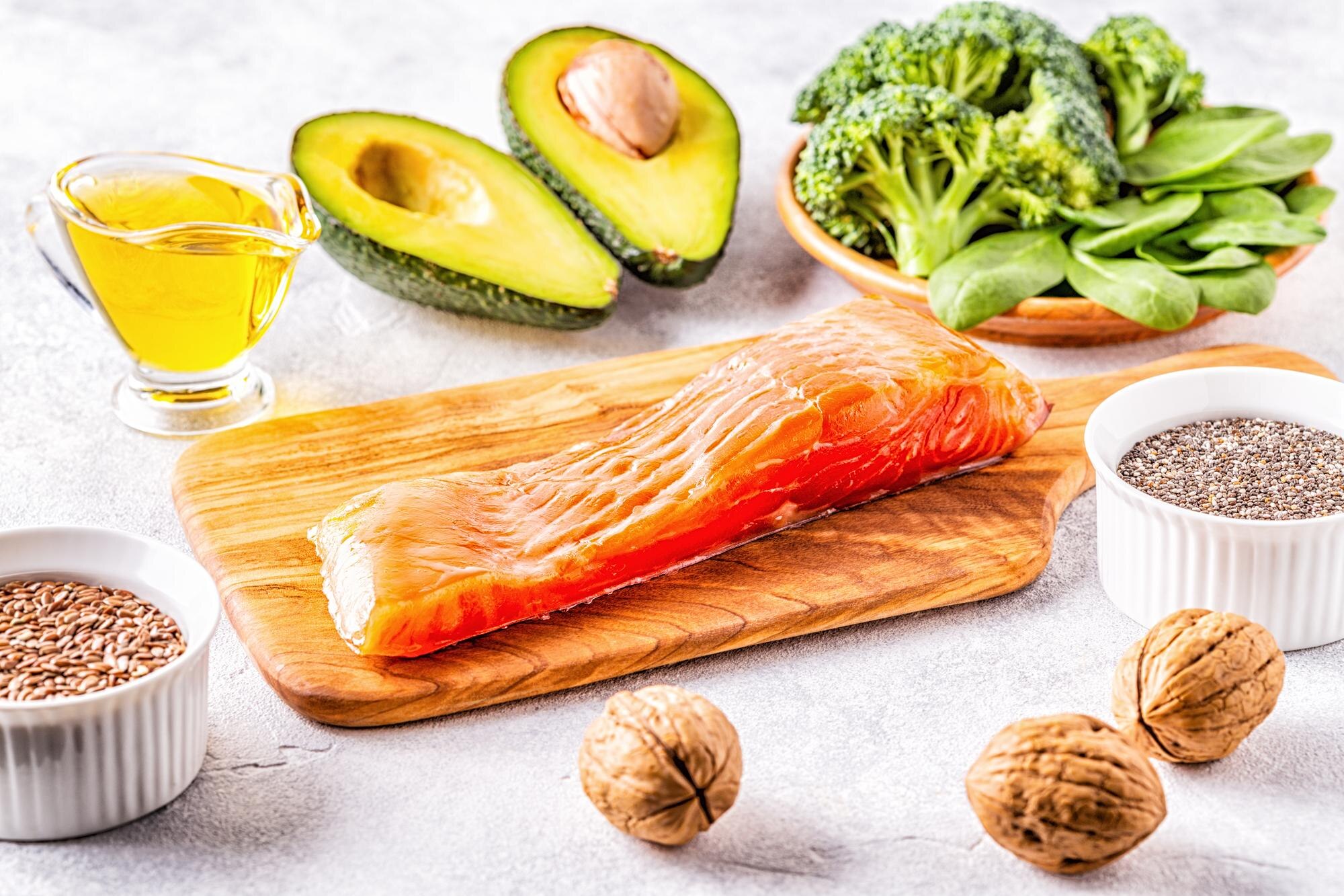 Selection of omega-3 rich foods including fresh salmon, walnuts, and flaxseeds arranged on a light background