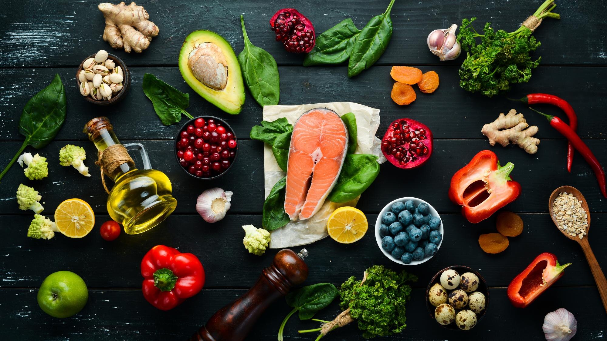 A flat-lay of anti-inflammatory foods including colourful vegetables, berries, nuts, seeds and oily fish on a light stone background