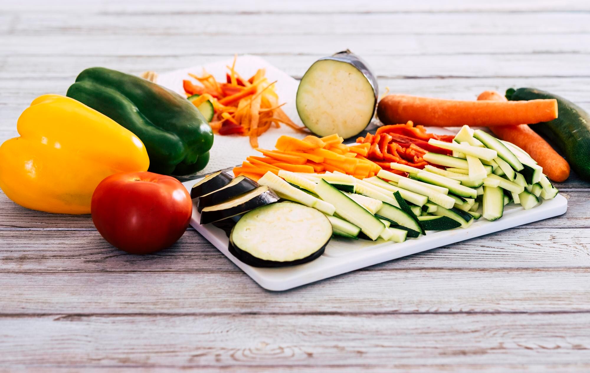 A colourful array of fresh low-FODMAP friendly vegetables including sliced carrots, courgette, aubergine, and peppers arranged on a wooden surface