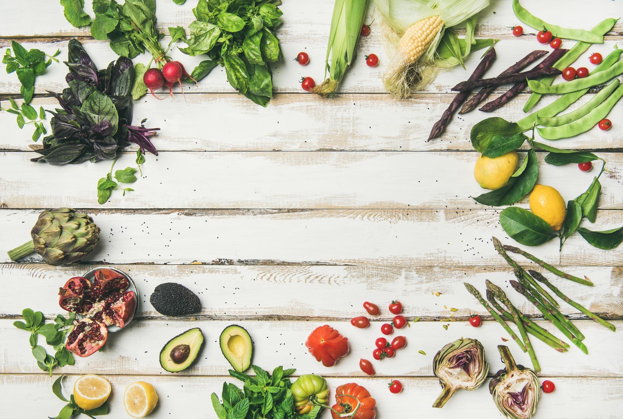 Colourful fresh vegetables and fruits arranged on a white wooden table — low-FODMAP friendly ingredients including kiwi, blueberries, carrots, and cucumber