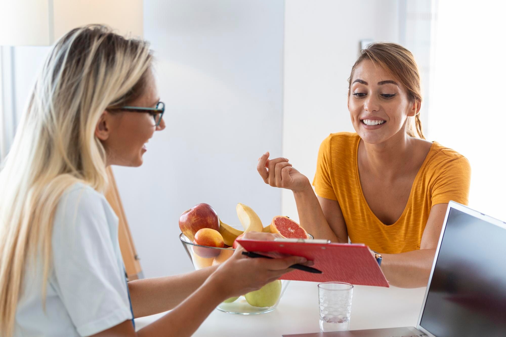 A nutritional therapist seated across from a client during a one-to-one consultation, reviewing notes together in a calm, light-filled room